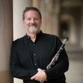 A man standing in a sandstone building holding a clarinet